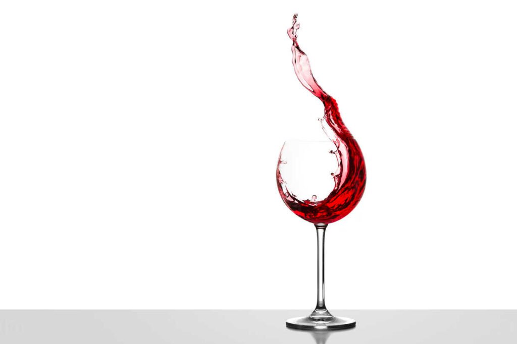 Red wine splashing in glass in front of white background